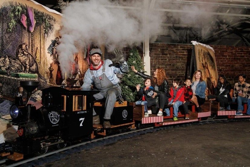 Dampfende Miniatureisenbahn mit Fahrgästen und verkleidetem Lokführer